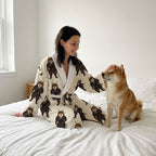 Woman wearing a robe with bear designs sitting on a bed with a dog.